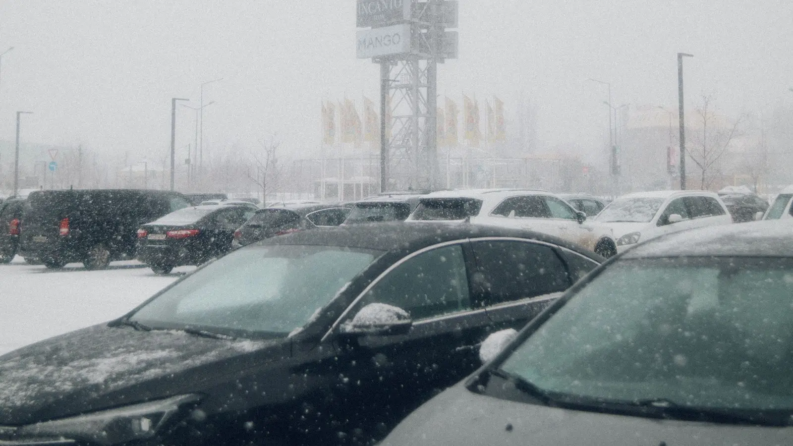 Snow-covered cars in a foggy shopping center parking lot