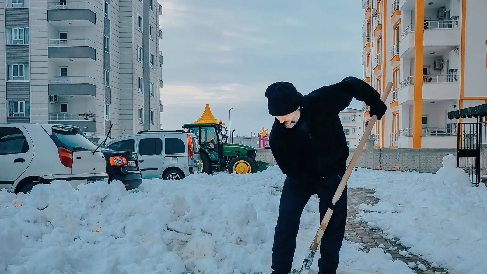 Man shoveling a snowbank beside apartment buildings