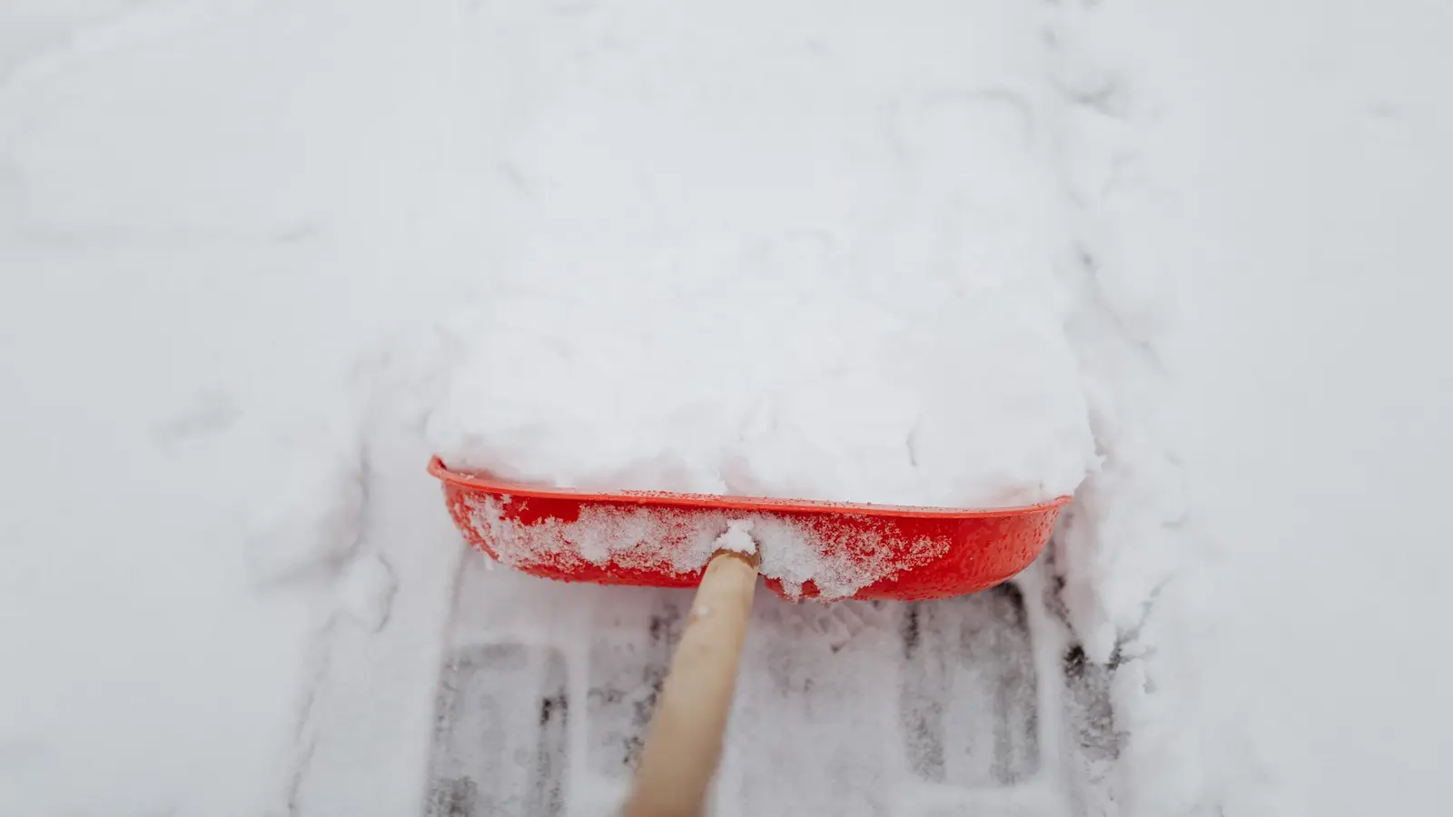 Close-up of a red shovel clearing snow from a driveway