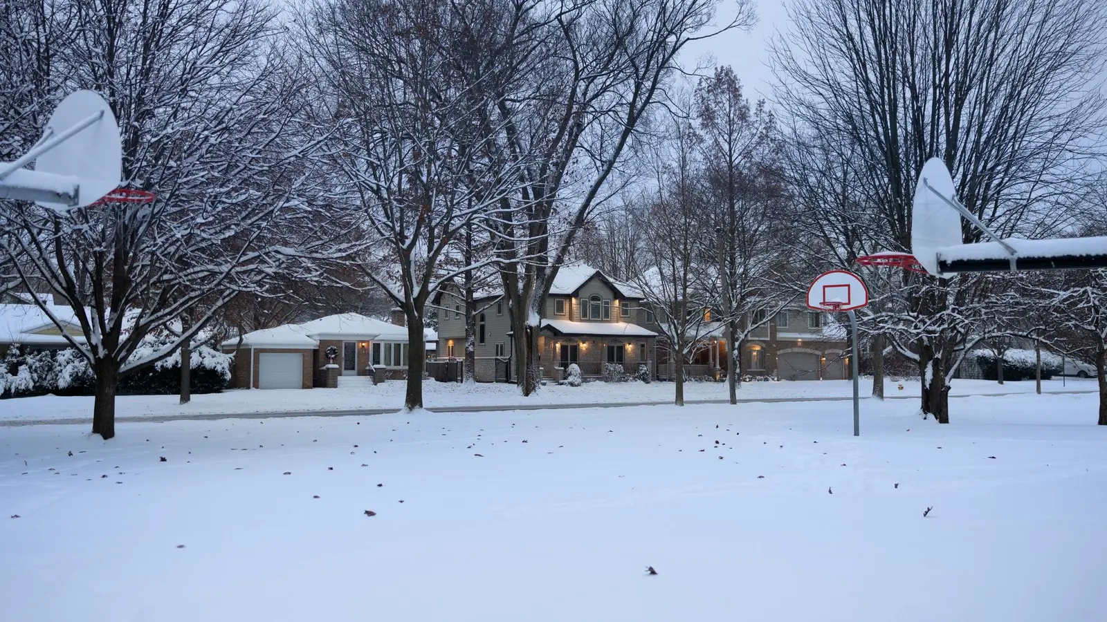 Snow-covered front yards and basketball hoops along a neighborhood street