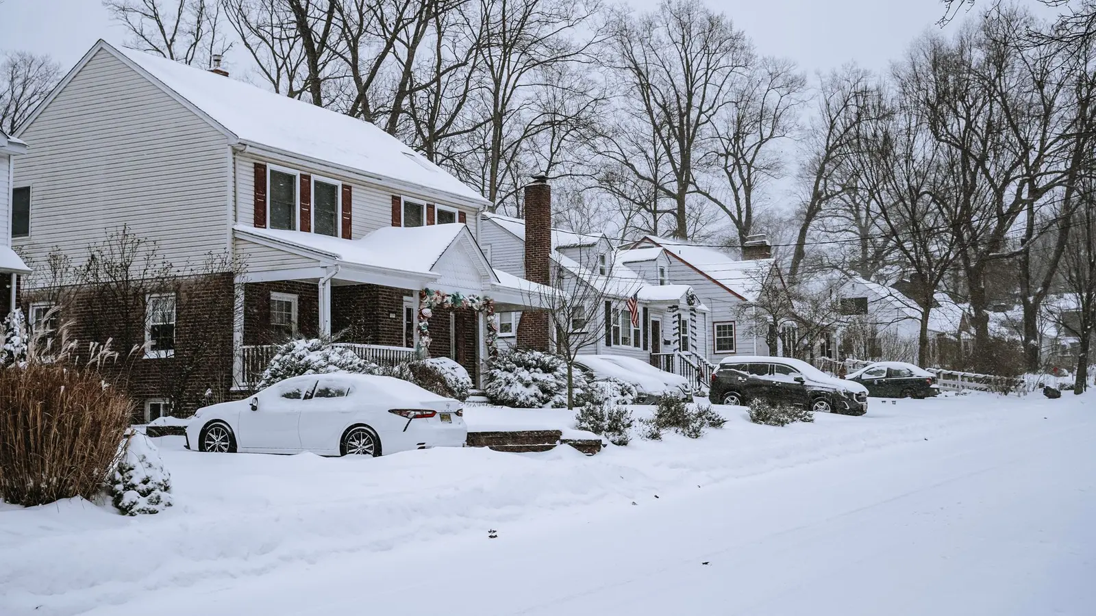 Snow-covered suburban street with two-story houses and parked cars