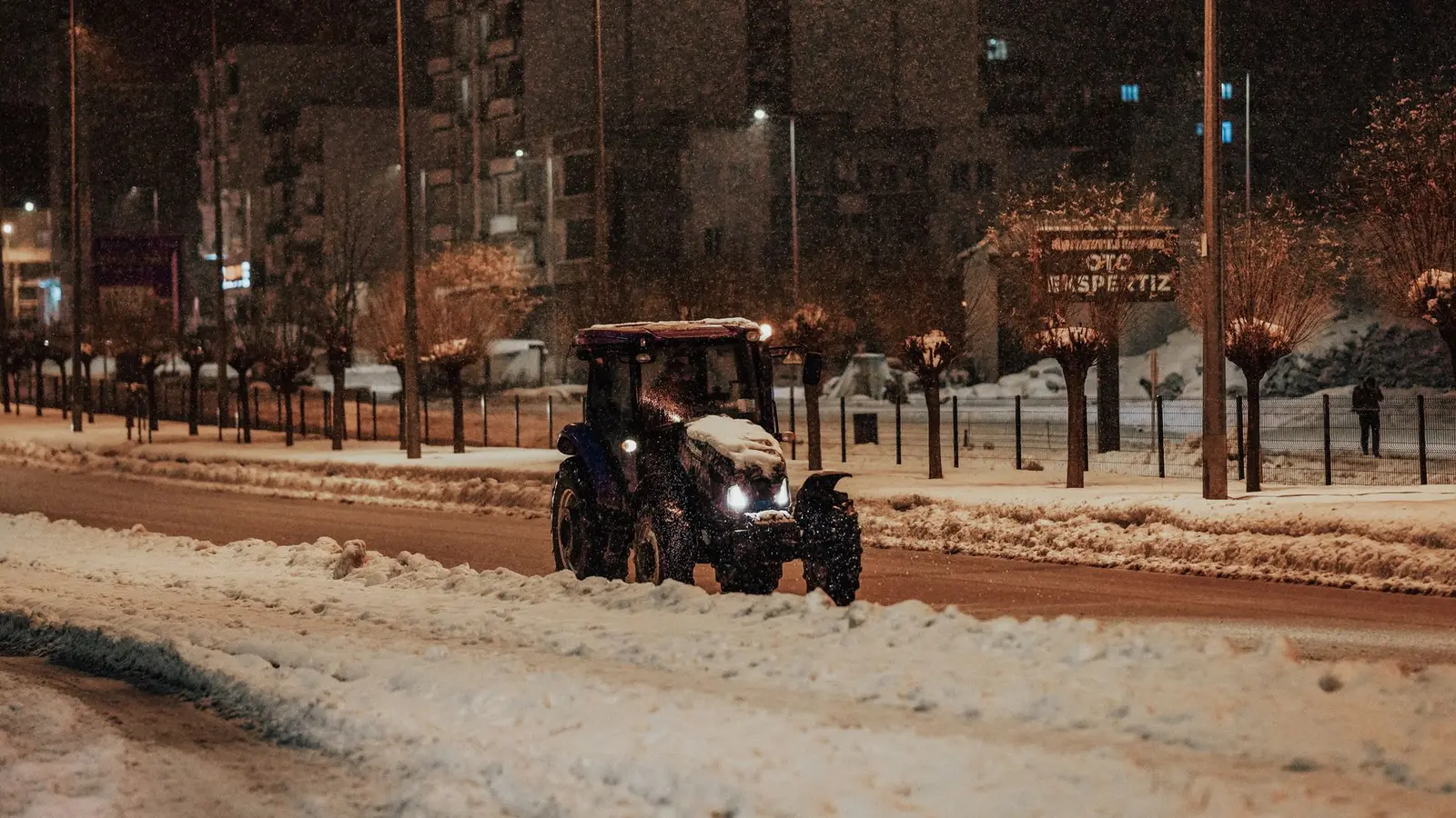 Tractor clearing a snowy street at night under streetlights