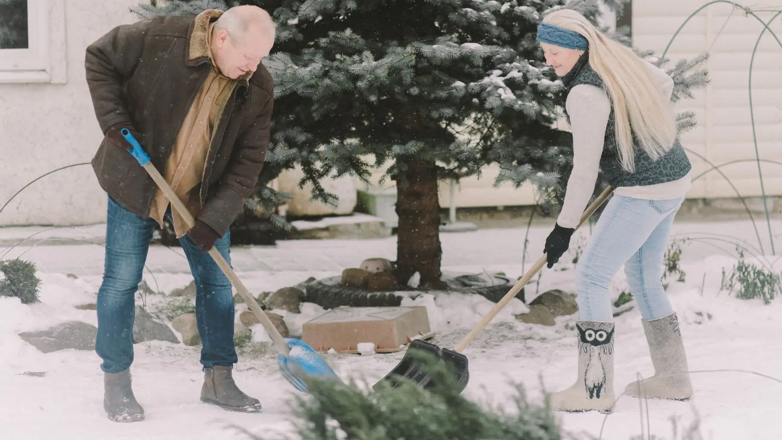 Two people shoveling snow in front of a house