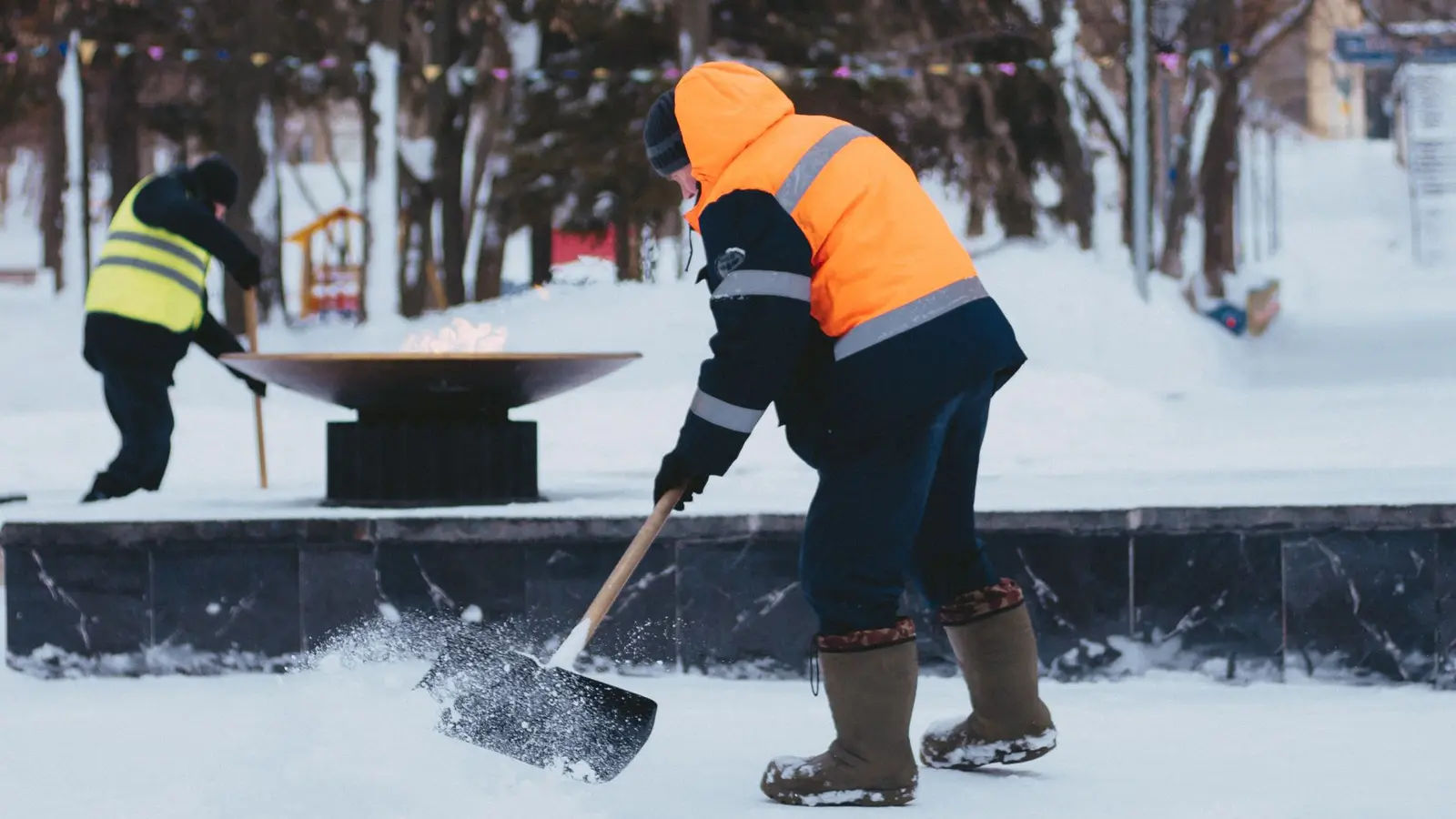 Workers in high-visibility jackets shoveling a snowy walkway